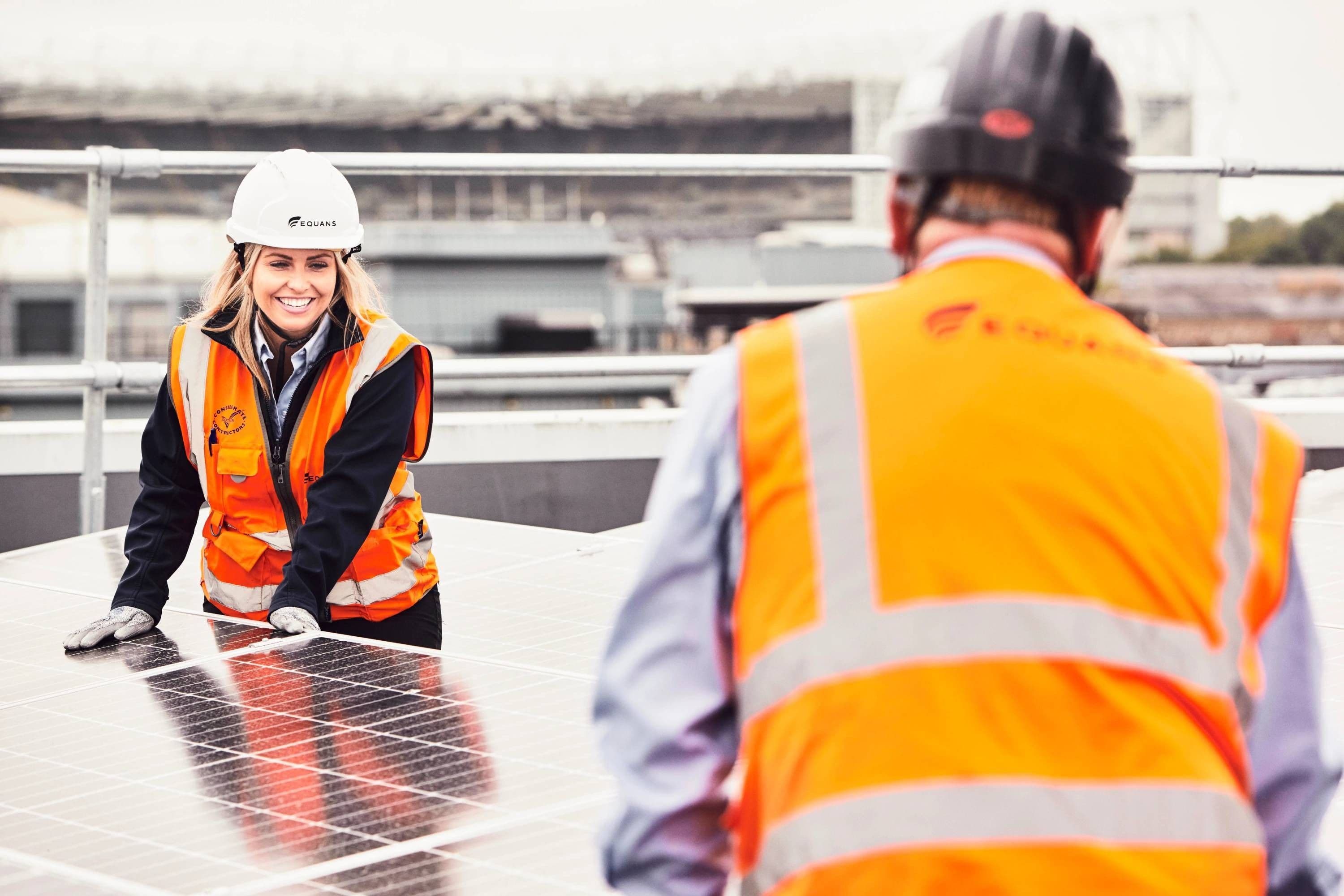 Two Equans colleagues in hi-vis jackets inspecting a rooftop solar array